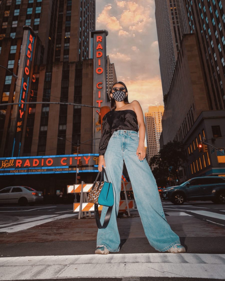 jessica wang wearing a patterned face mask, a silk one shoulder top, and wide leg denim jeans while sharing her essential items for traveling // Jessica Wang - Notjessfashion.com